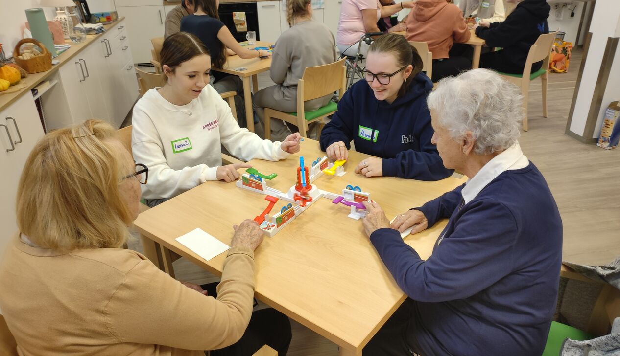 Junge und ältere Menschen spielen gemeinsam an einem Tisch mit einem Spielzeug in einem freundlichen, sozialen Umfeld.