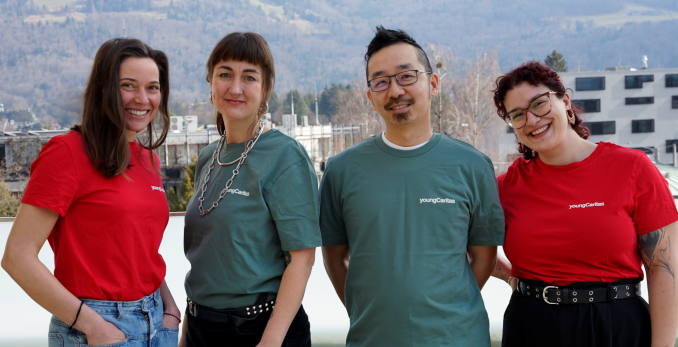 Eine Gruppe von vier Personen in T-Shirts mit dem Logo von Junge Caritas posiert vor einer bergigen Kulisse.