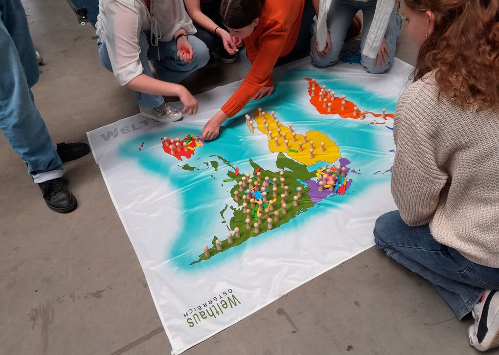 Eine Gruppe von Personen interagiert mit einer großen Weltkarte, die mit farbigen Spielfiguren markiert ist.