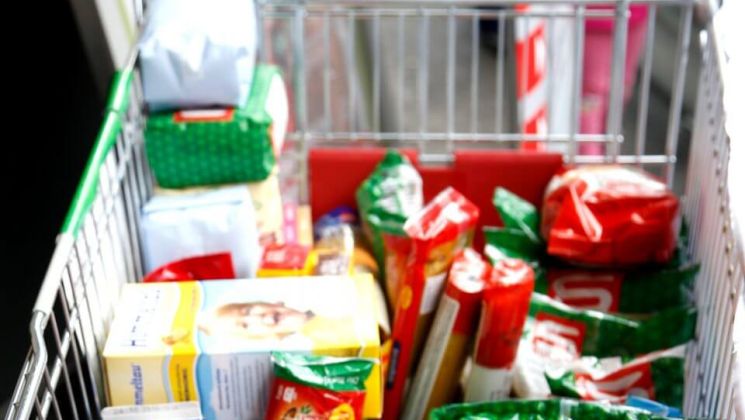 Ein Einkaufswagen, gefüllt mit verschiedenen Lebensmitteln und Packungen im Supermarkt.