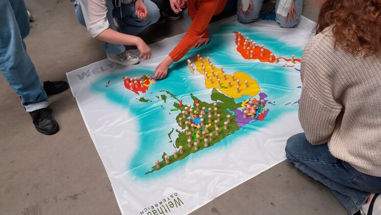 Eine Gruppe von Personen interagiert mit einer großen Weltkarte, die mit farbigen Spielfiguren markiert ist.