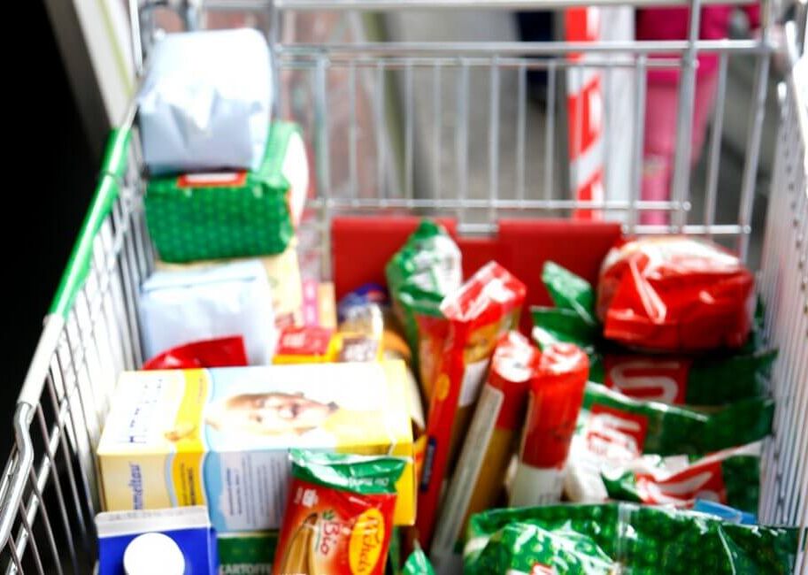Ein Einkaufswagen, gefüllt mit verschiedenen Lebensmitteln und Packungen im Supermarkt.