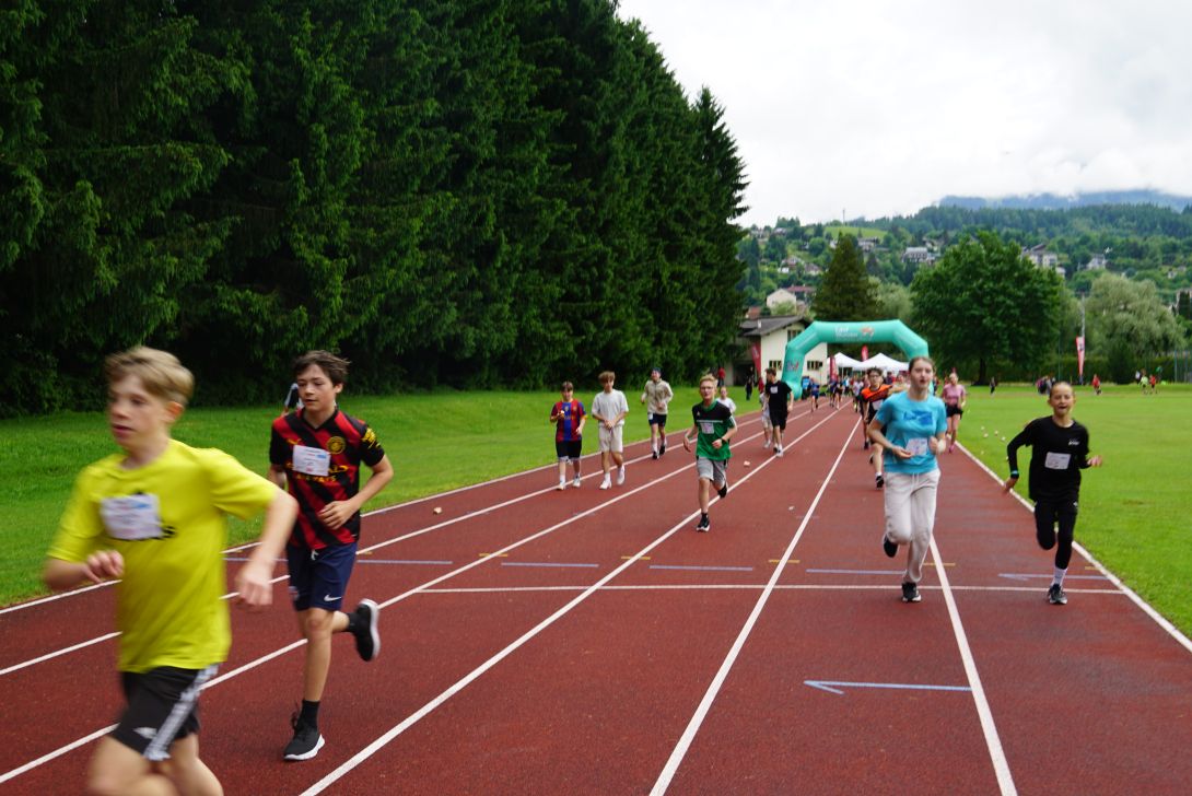 Eine Gruppe von Schülern läuft auf einer Laufbahn während eines Wettbewerbs, umgeben von Bäumen und einer Sporteinrichtung.