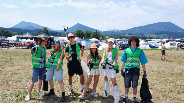 6 jugendliche mit grünen Sicherheitswesten bereit für Müllsammlung auf einem Festivalgelände.