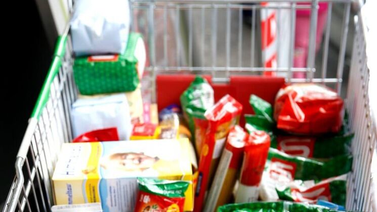 Ein Einkaufswagen, gefüllt mit verschiedenen Lebensmitteln und Packungen im Supermarkt.